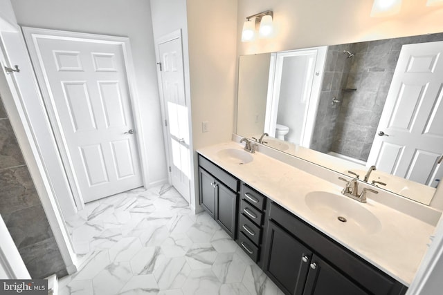 bathroom featuring double vanity, marble finish floor, a tile shower, and a sink