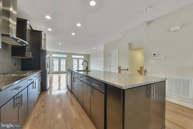 20765 Duxbury Ter, Ashburn, VA 20147 - kitchen with wall chimney range hood, stainless steel appliances, light wood finished floors, a large island, and light stone countertops