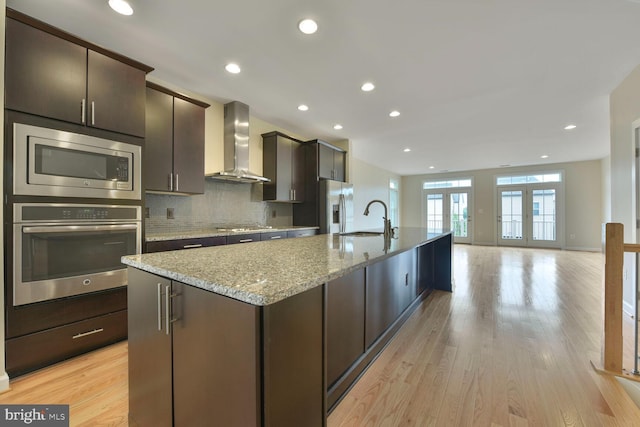 20765 Duxbury Ter, Ashburn, VA 20147 - kitchen with stainless steel appliances, wall chimney exhaust hood, a spacious island, backsplash, and light wood finished floors