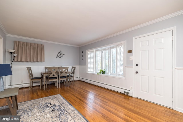 dining space with a baseboard heating unit, ornamental molding, hardwood / wood-style floors, and wainscoting