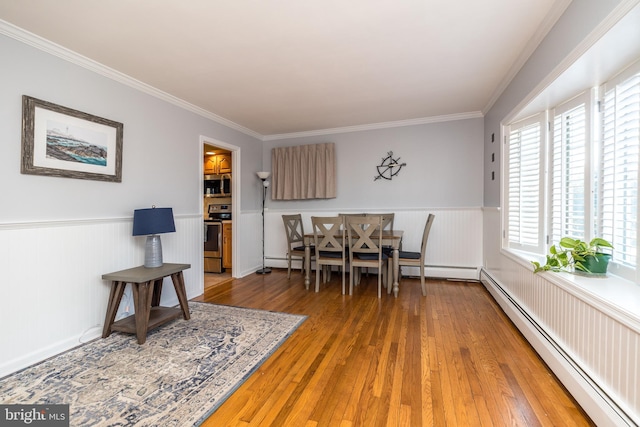 dining room featuring a baseboard heating unit, wainscoting, wood-type flooring, and crown molding