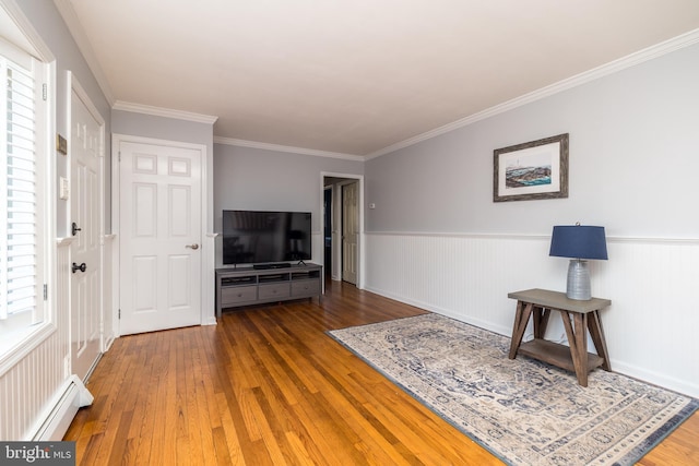 living room featuring a wainscoted wall, hardwood / wood-style floors, baseboard heating, and crown molding