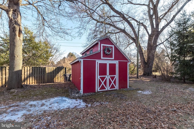 snow covered structure with a storage unit, fence, and an outbuilding