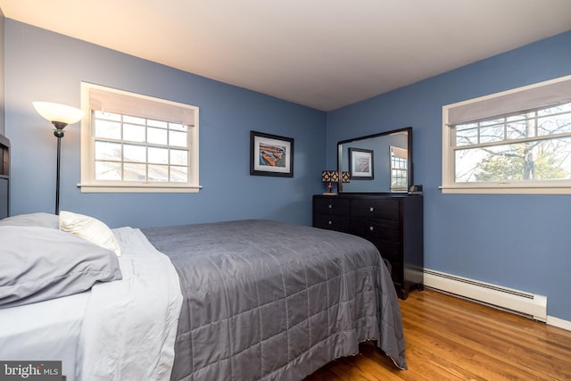 bedroom featuring a baseboard heating unit, baseboards, and wood finished floors