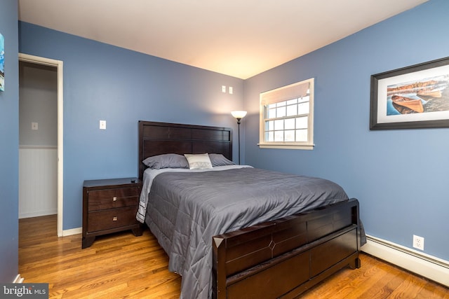 bedroom with a wainscoted wall, a baseboard radiator, and light wood-style flooring