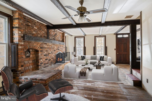 living room with ceiling fan, a brick fireplace, wood-type flooring, and beam ceiling