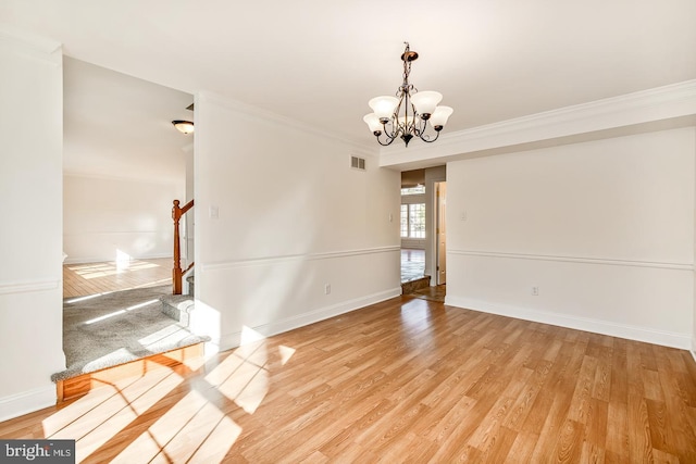 empty room featuring an inviting chandelier, crown molding, and light hardwood / wood-style floors