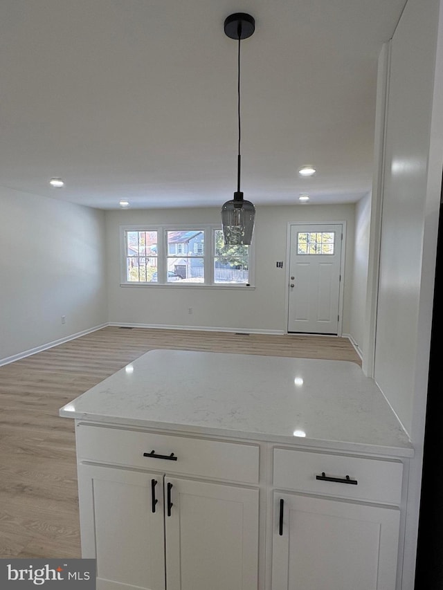 kitchen featuring decorative light fixtures, light wood-style flooring, open floor plan, white cabinets, and light stone countertops