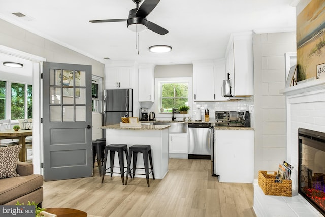 kitchen featuring a kitchen island, stainless steel appliances, a fireplace, light stone countertops, and white cabinets