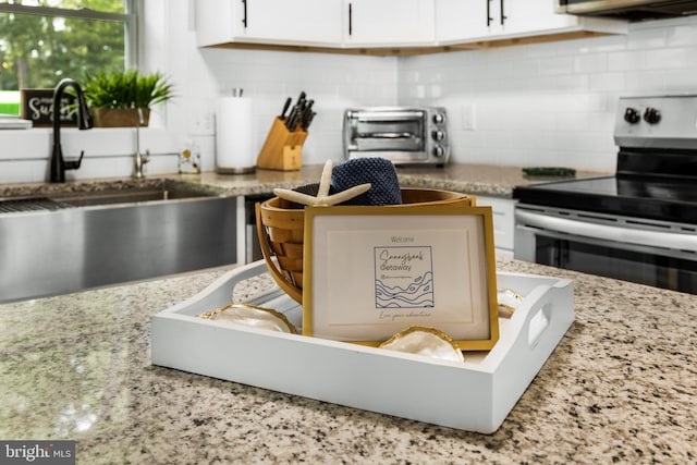 kitchen featuring backsplash, electric range, sink, and white cabinets