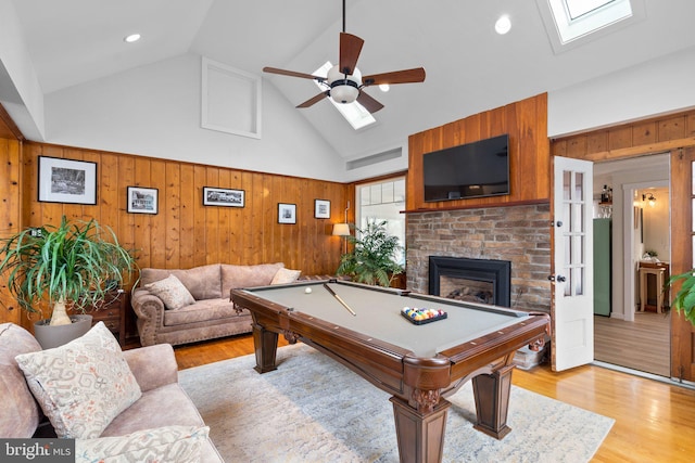 rec room with a skylight, a fireplace, high vaulted ceiling, and light wood finished floors