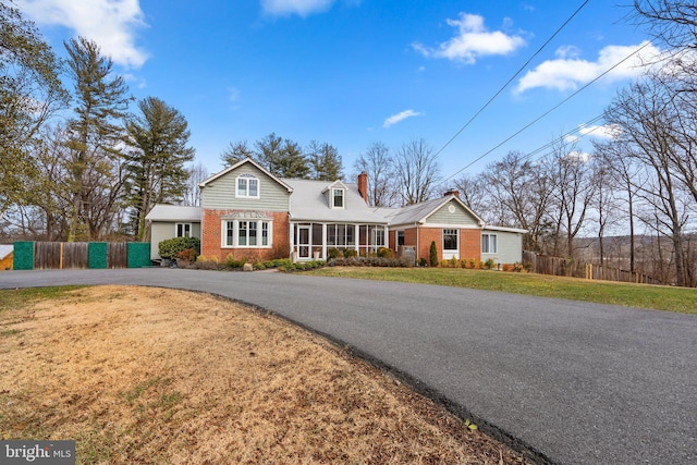 traditional-style house featuring aphalt driveway, brick siding, fence, a chimney, and a front yard