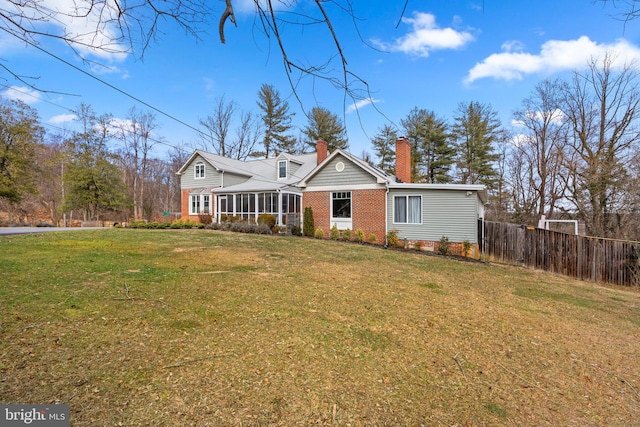 view of front of house with brick siding, fence, a sunroom, a front lawn, and a chimney