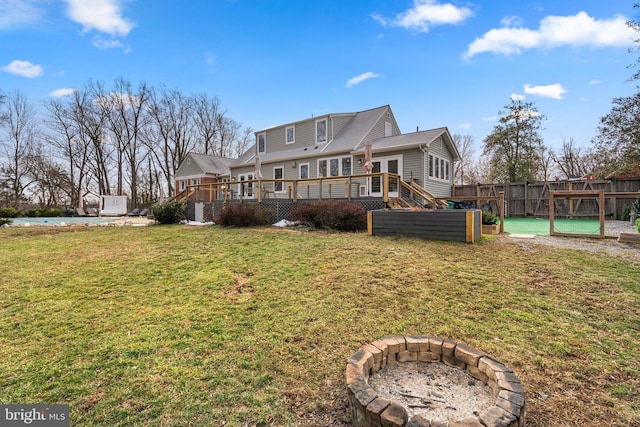 rear view of property featuring a deck, a yard, a fire pit, and fence