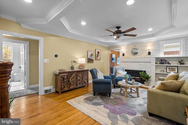 living area featuring light wood-style floors, visible vents, a raised ceiling, and ornamental molding