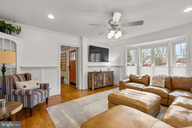 living area with light wood-type flooring, a ceiling fan, crown molding, and wainscoting