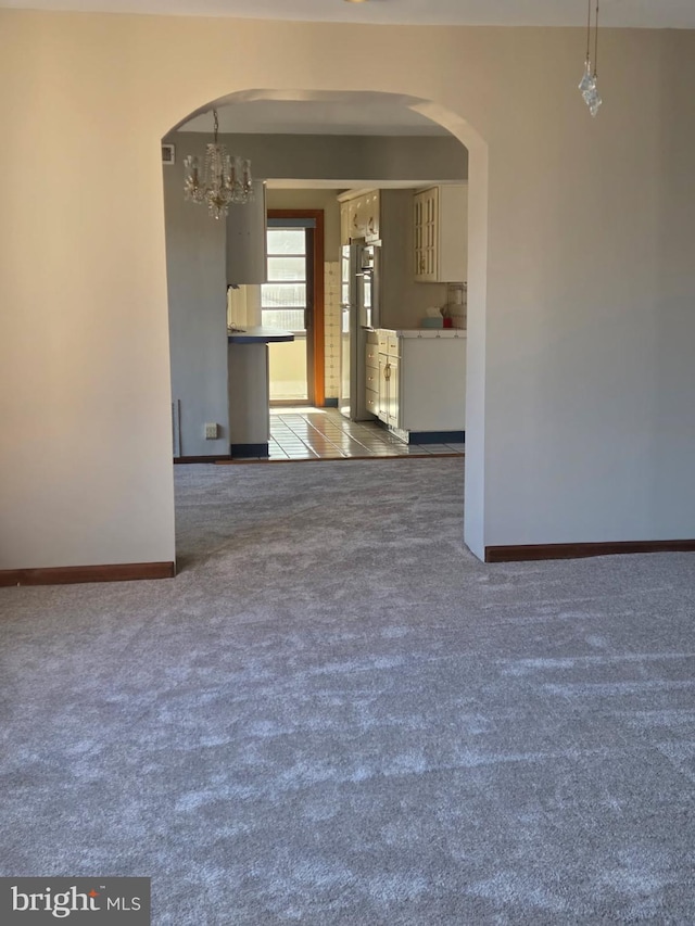 empty room with light carpet, arched walkways, and baseboards