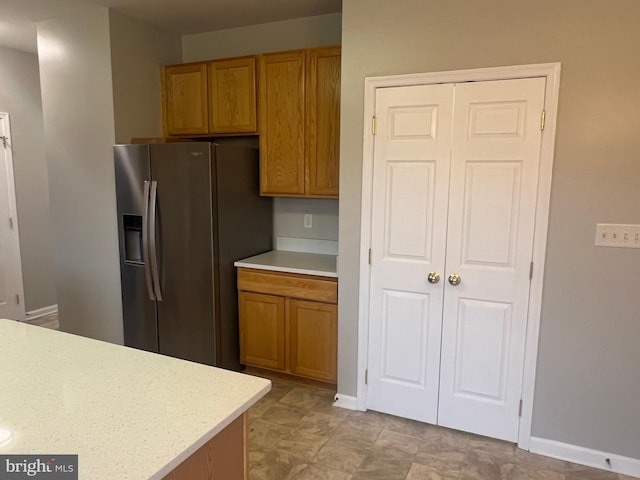 kitchen with light countertops, stainless steel fridge with ice dispenser, brown cabinets, and baseboards