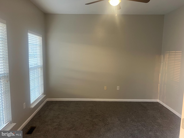 spare room featuring dark colored carpet, visible vents, plenty of natural light, and a ceiling fan