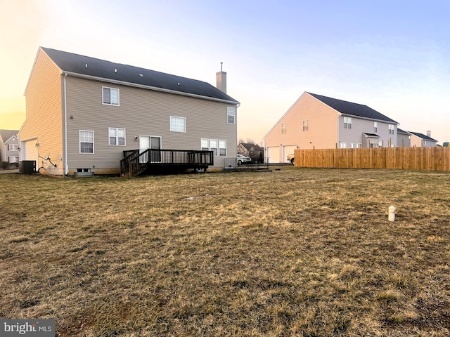 back of house at dusk featuring central AC unit, fence, a wooden deck, a yard, and a chimney