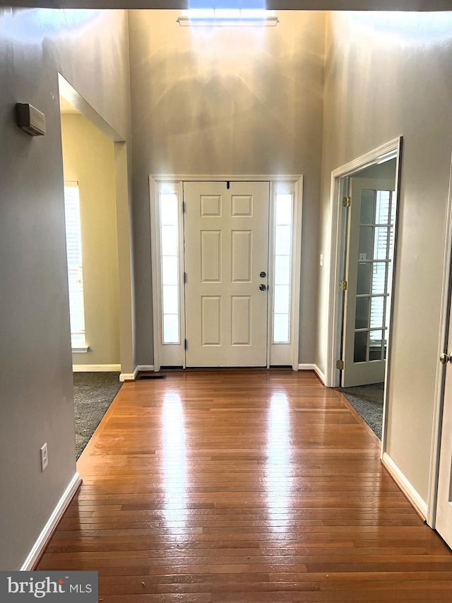 foyer featuring baseboards, wood finished floors, and a towering ceiling