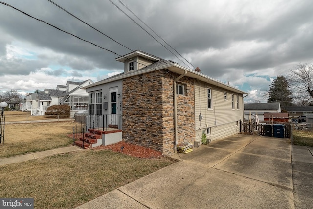 view of property exterior featuring stone siding, a yard, and fence