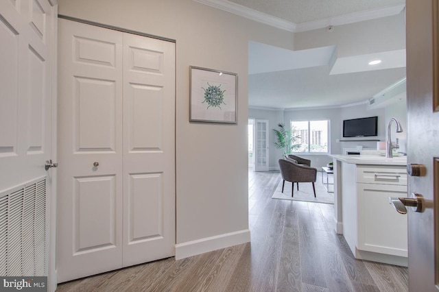 corridor featuring visible vents, light wood-style flooring, ornamental molding, a sink, and baseboards