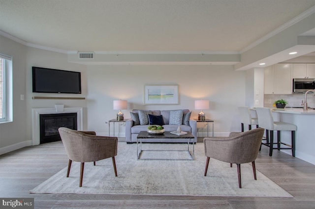 living room with light wood-type flooring, a glass covered fireplace, visible vents, and crown molding