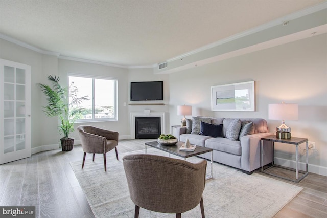 living area featuring baseboards, light wood-type flooring, visible vents, and crown molding