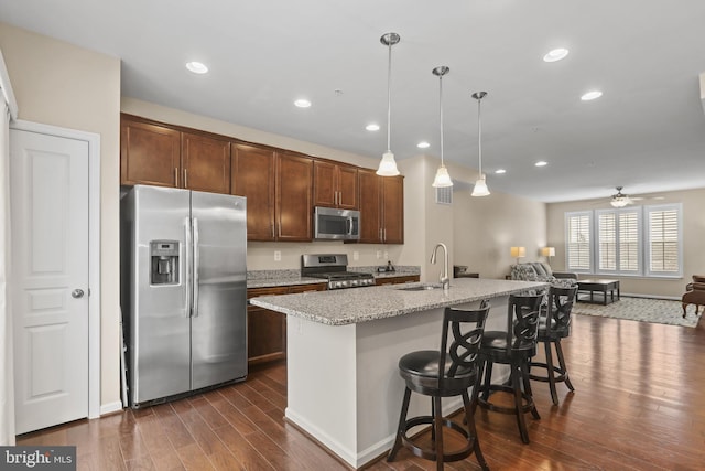 kitchen with appliances with stainless steel finishes, decorative light fixtures, sink, a breakfast bar area, and a kitchen island with sink