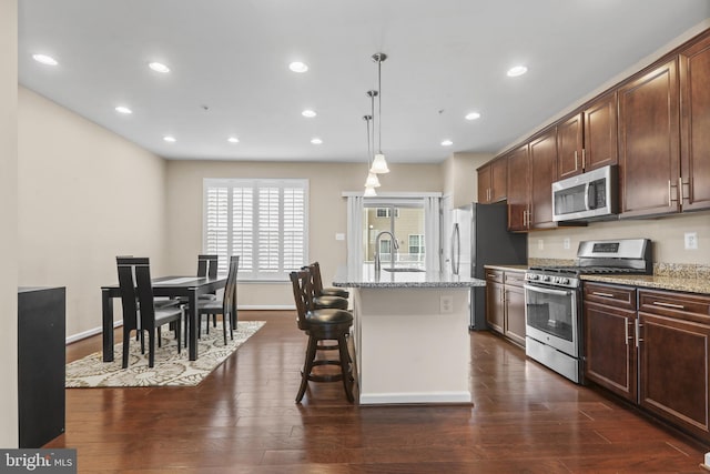 kitchen with sink, light stone counters, hanging light fixtures, an island with sink, and stainless steel appliances