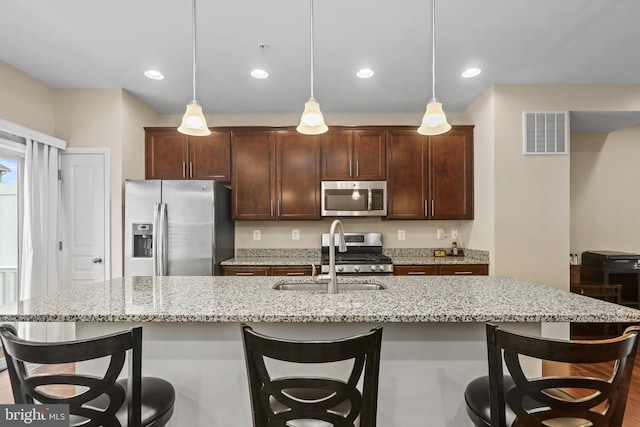 kitchen featuring appliances with stainless steel finishes, sink, hanging light fixtures, and a center island with sink