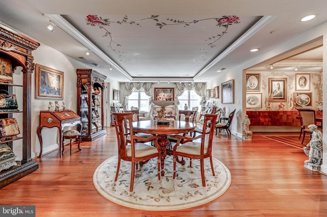 dining space with light wood finished floors, baseboards, crown molding, and a raised ceiling