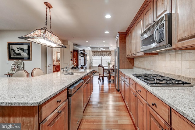 kitchen with stainless steel appliances, tasteful backsplash, a sink, light wood-style floors, and hanging light fixtures