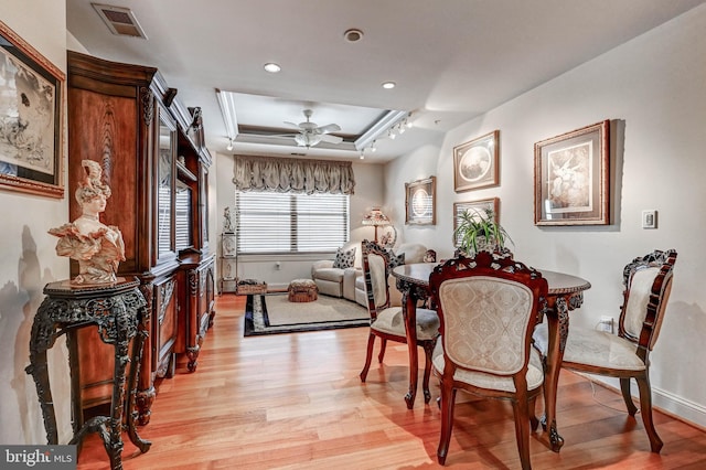 dining room featuring a ceiling fan, a tray ceiling, light wood-style floors, and visible vents