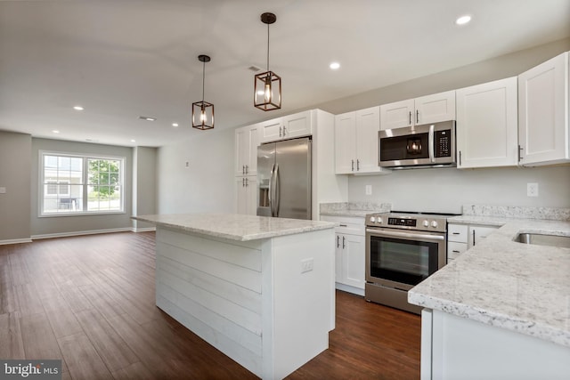 kitchen featuring white cabinetry, decorative light fixtures, a center island, appliances with stainless steel finishes, and light stone countertops