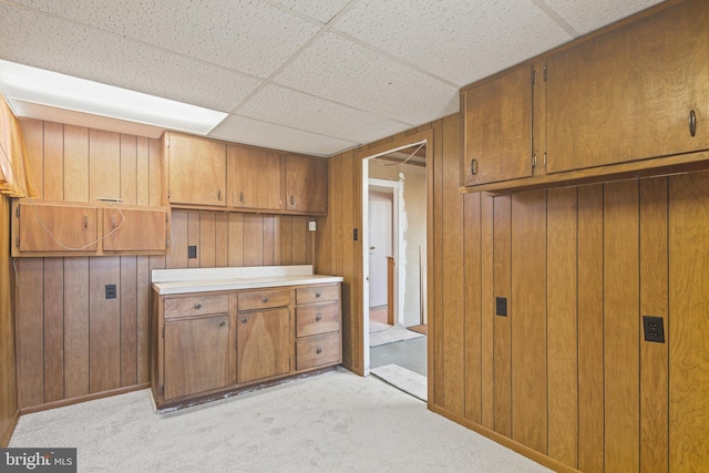 kitchen featuring wooden walls, light colored carpet, and brown cabinets