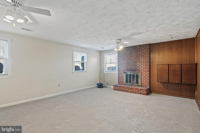 unfurnished living room with ceiling fan, carpet floors, a fireplace, visible vents, and baseboards