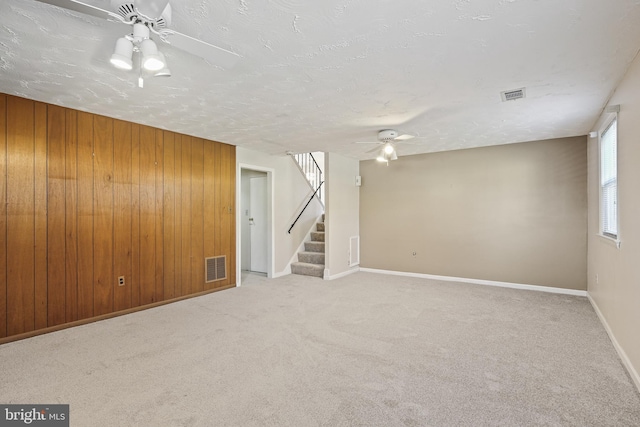 below grade area featuring stairway, visible vents, a ceiling fan, and wood walls