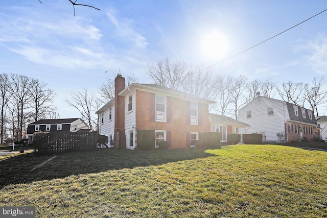 view of property exterior with brick siding, fence, a chimney, and a lawn