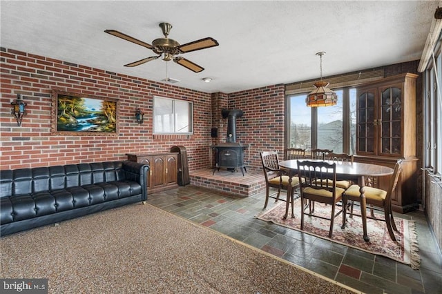 living room featuring ceiling fan, brick wall, a textured ceiling, and a wood stove