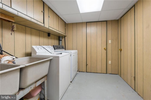 clothes washing area featuring cabinets, washing machine and clothes dryer, and wood walls