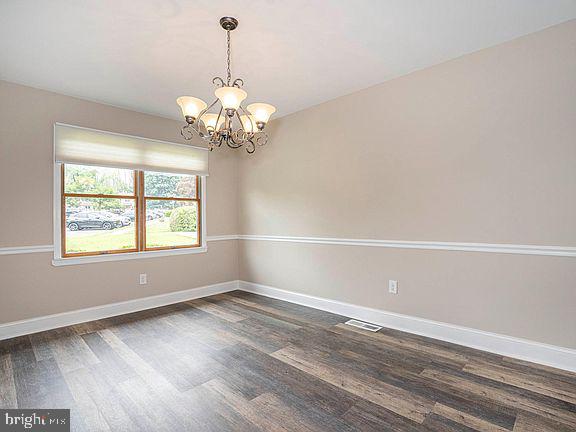 unfurnished room featuring baseboards, dark wood-style flooring, visible vents, and an inviting chandelier