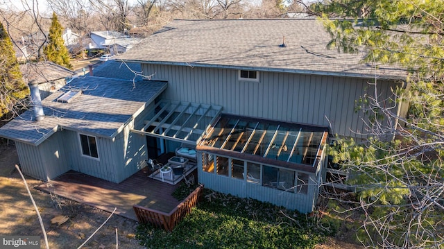 rear view of house with a shingled roof, a wooden deck, and a sunroom