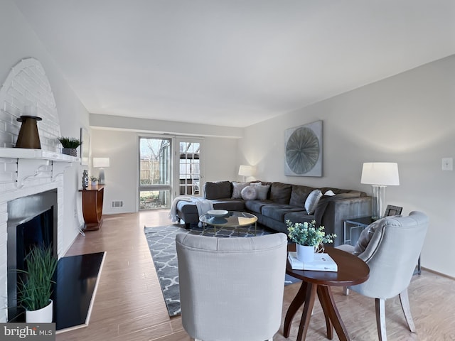 living area featuring a brick fireplace, light wood-style flooring, and visible vents