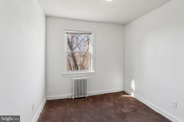 spare room with radiator, baseboards, and dark carpet