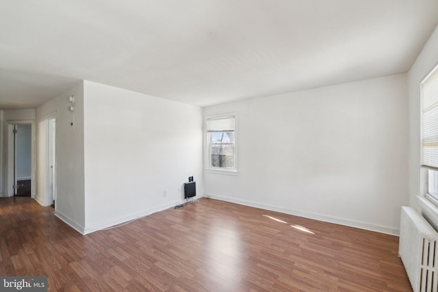 unfurnished room with baseboards, radiator heating unit, and wood finished floors