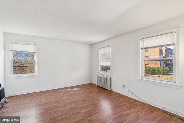 unfurnished room with plenty of natural light, radiator heating unit, baseboards, and wood finished floors