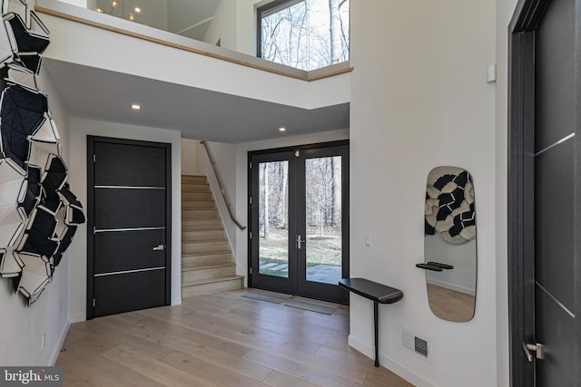 foyer featuring light hardwood / wood-style flooring, french doors, a healthy amount of sunlight, and a high ceiling