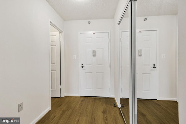 foyer entrance with a textured ceiling, dark wood finished floors, and baseboards